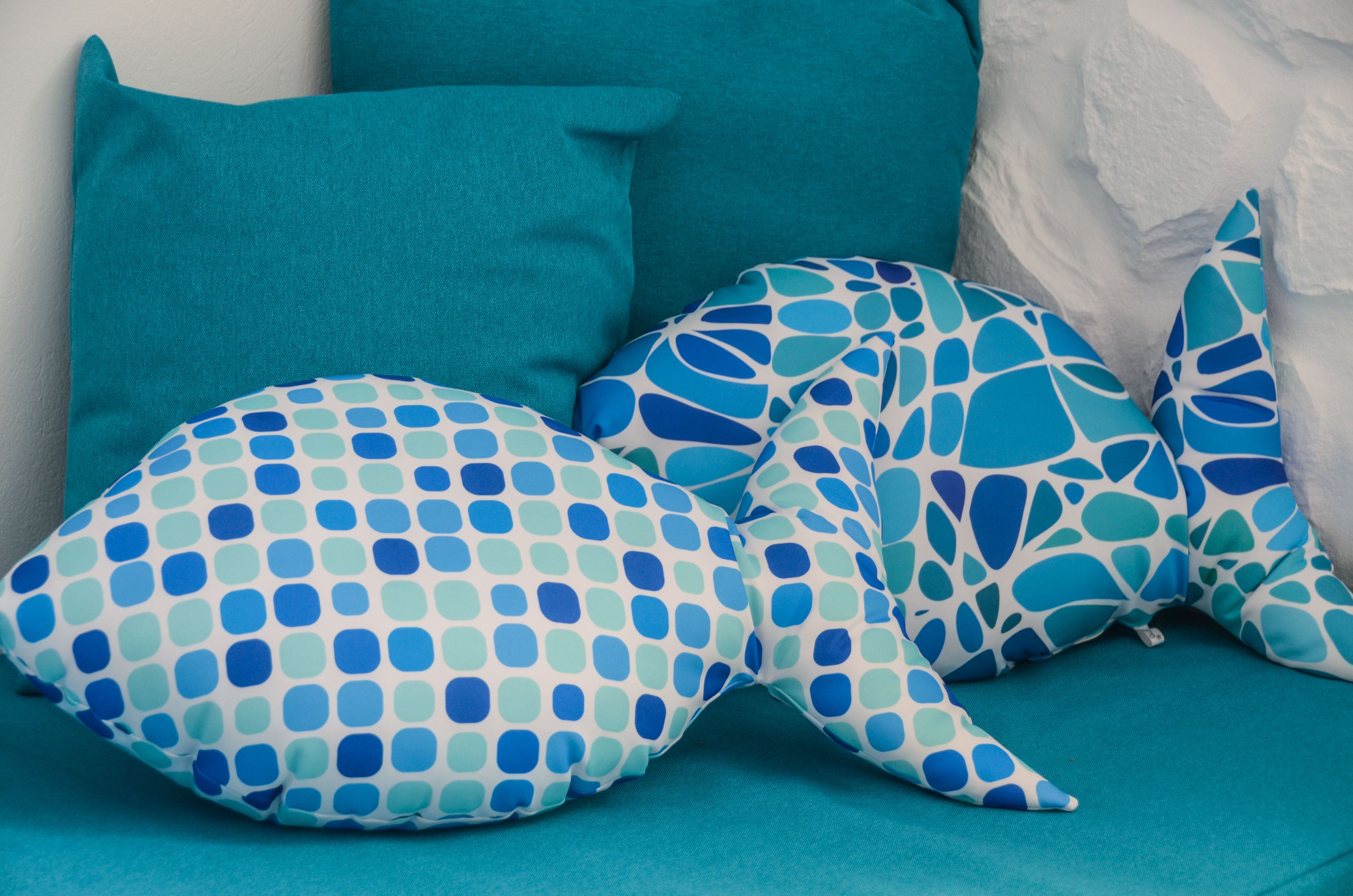 A teal-colored sofa with three cushions, one with a blue and white polka dot pattern and two with a blue abstract design.