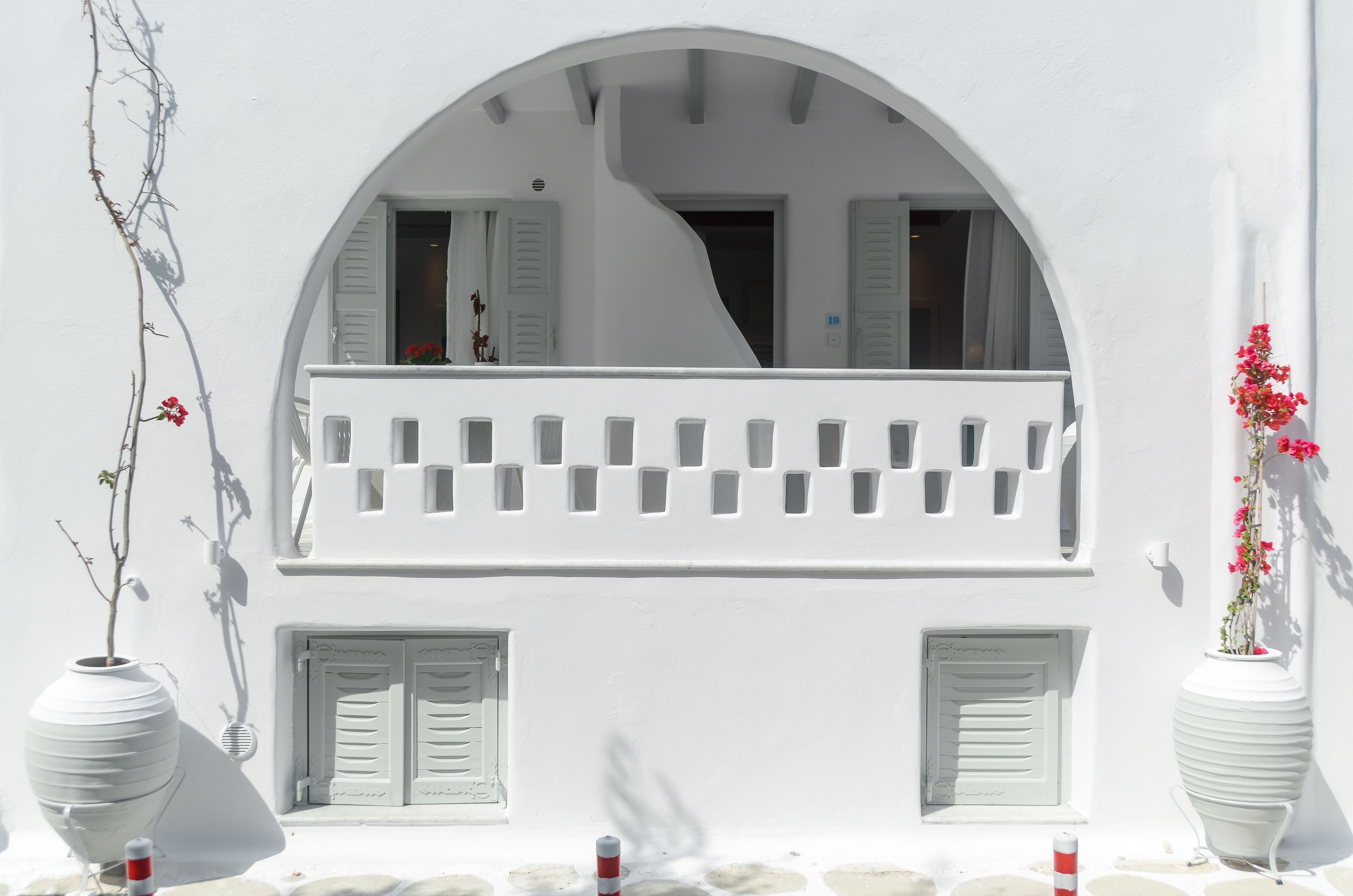 Un edificio blanco con balcón, contraventanas y plantas en macetas.