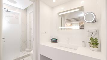 Un baño moderno con ducha, lavamanos con espejo y una planta en maceta.