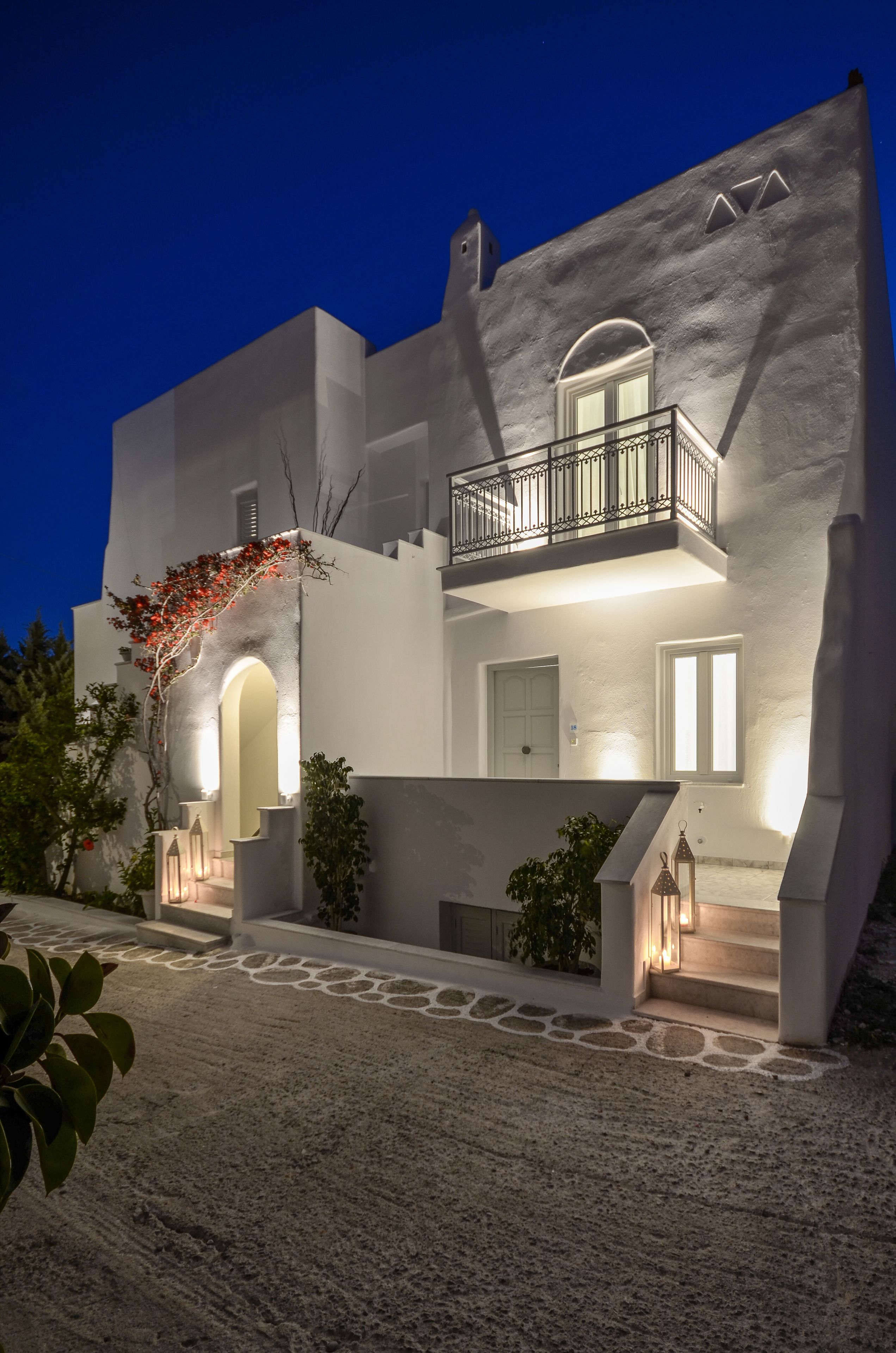 A modern building with a white facade, a balcony, and a stone pathway leading to the entrance.