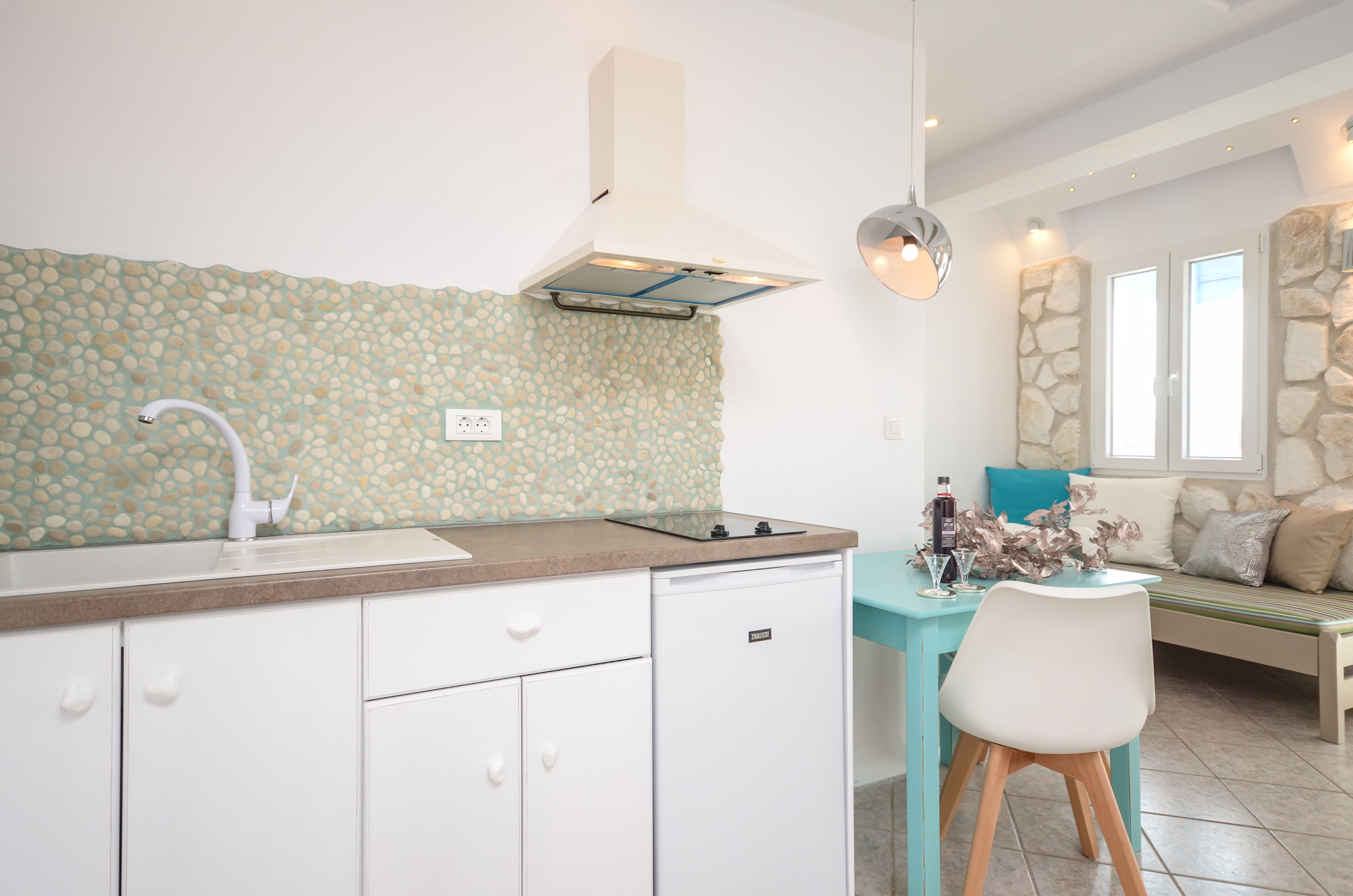 Cocina moderna con salpicadero de piedra, armarios blancos y una zona de comedor con banco y mesa.