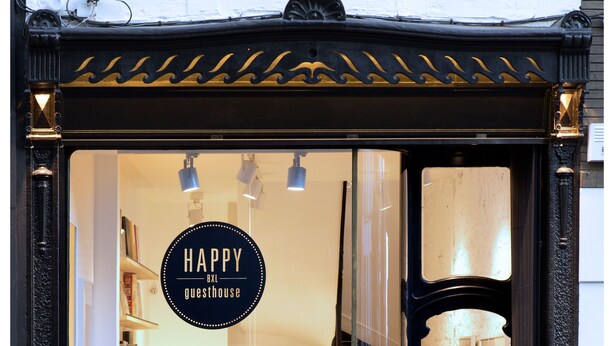A storefront with a sign reading "HAPPY GUESTHOUSE" and a display window showcasing a bed and pillows. - HAPPY Guesthouse (Brussels)