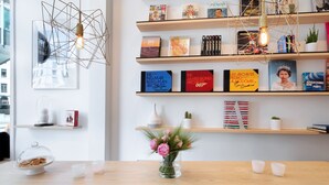A modern interior with a wooden bookshelf, decorative light fixtures, and a clear vase with flowers on a wooden table. - HAPPY Guesthouse (Brussels)