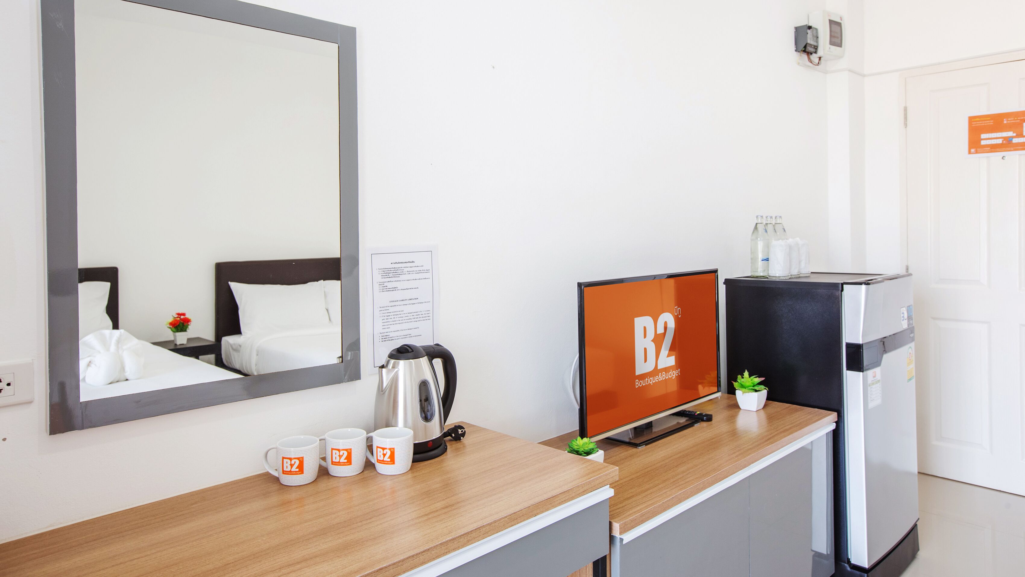 Habitación de hotel con cama, escritorio con cafetera, cartel de B2 Boutique & Budget, refrigerador y espejo.