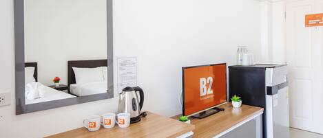 Habitación de hotel con cama, escritorio con cafetera, cartel de B2 Boutique & Budget, refrigerador y espejo.