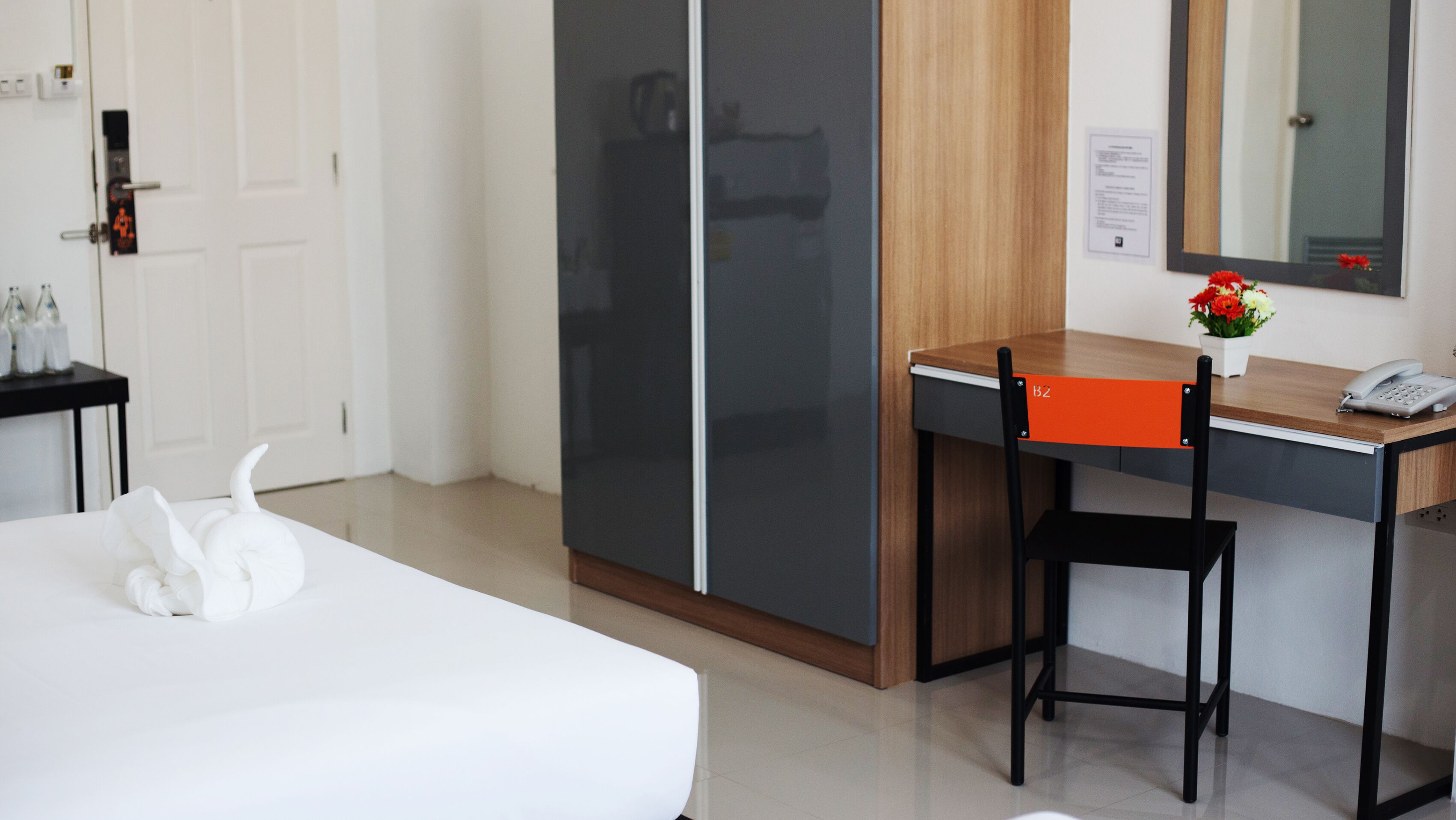 A hotel room with a bed, a desk with a chair, a telephone, and a mirror on the wall.