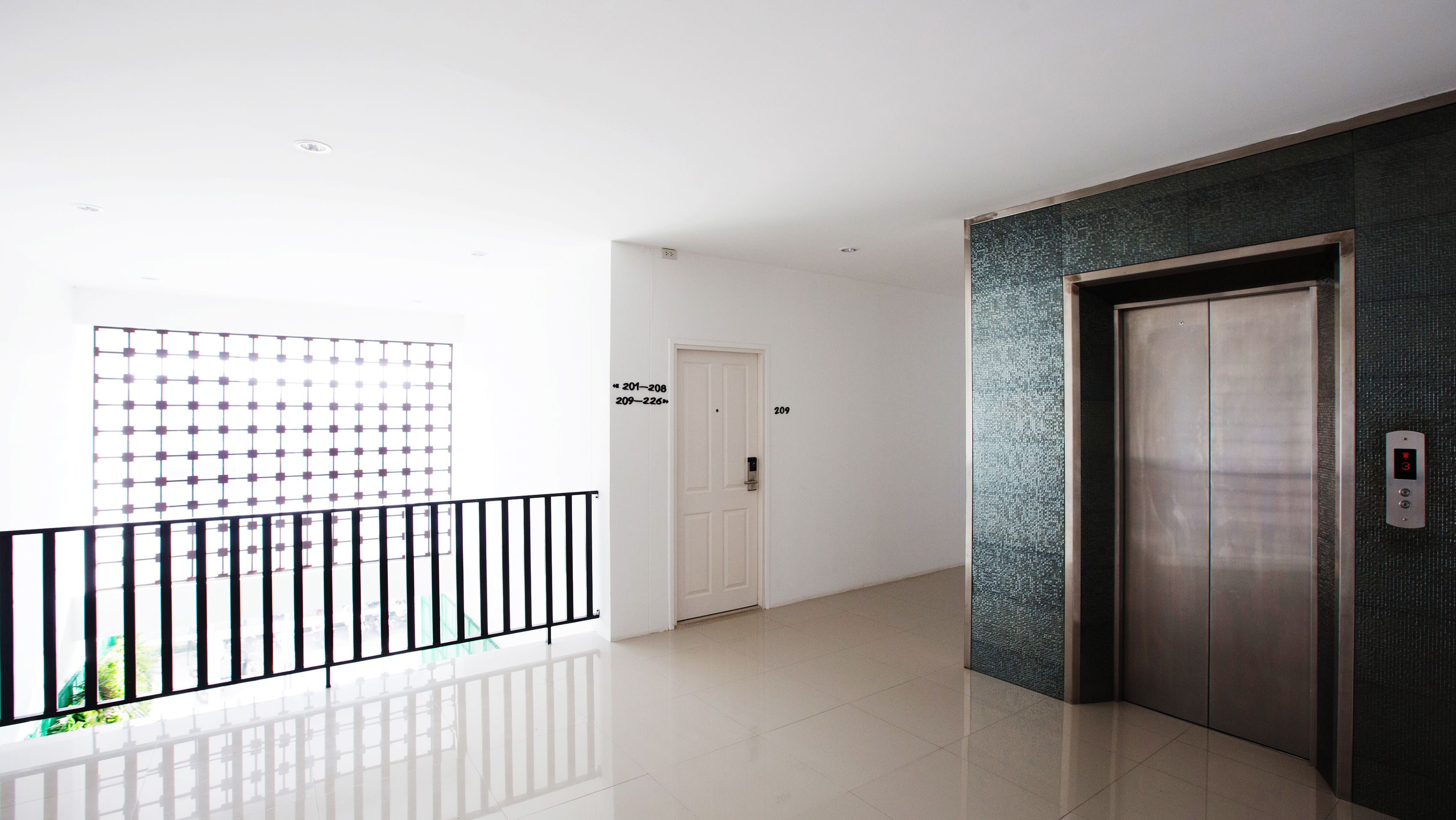 A modern hallway with a glass railing, a door labeled "209", and an elevator.