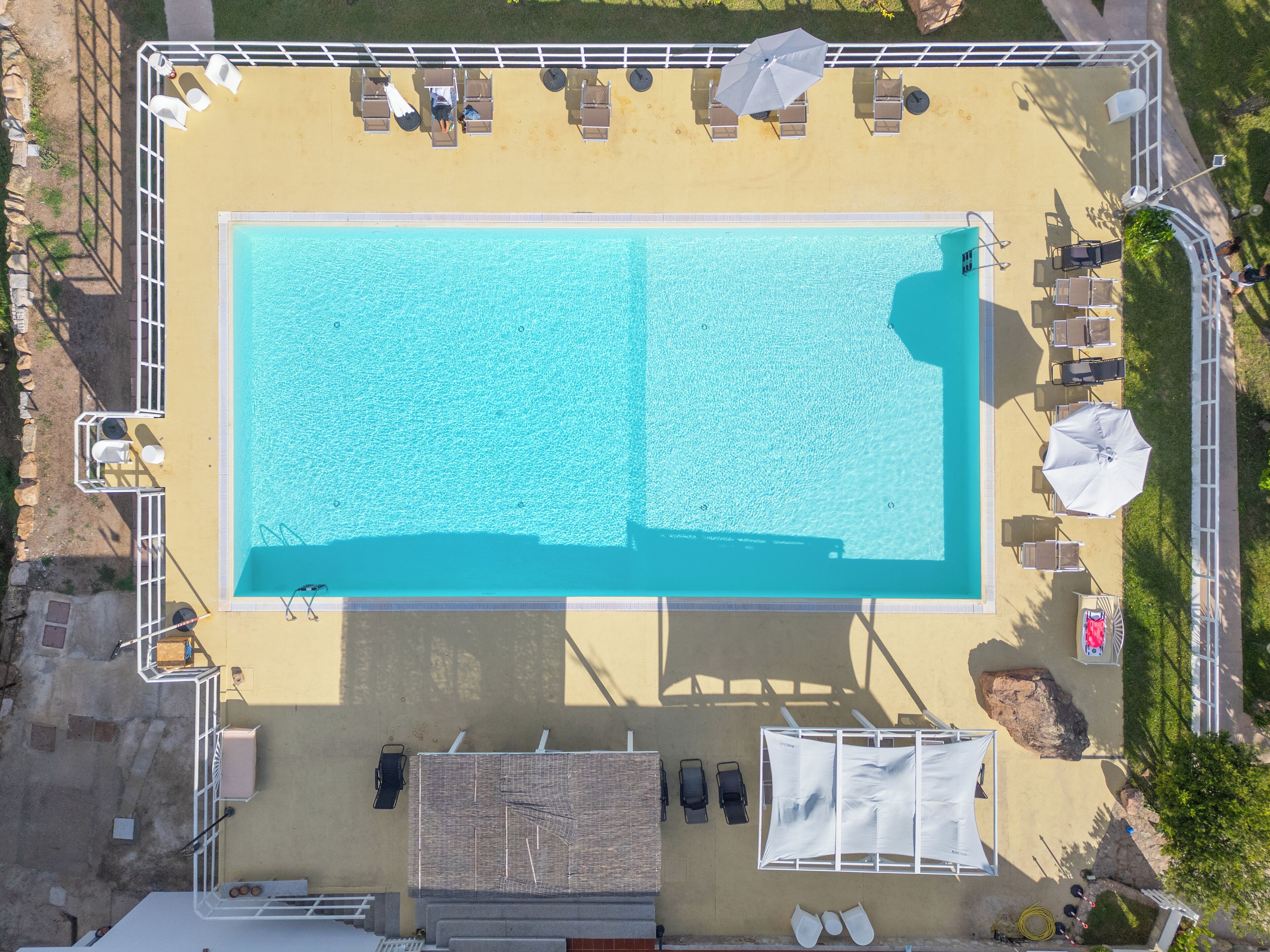 An aerial view of a swimming pool with lounge chairs and umbrellas, surrounded by a deck and a small garden area.