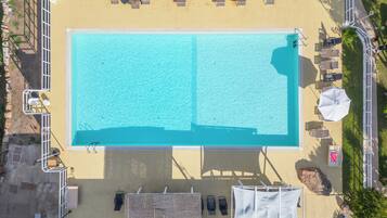 An aerial view of a swimming pool with lounge chairs and umbrellas, surrounded by a deck and a small garden area.