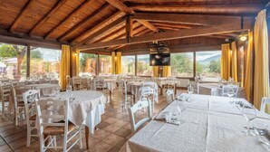 Un restaurant avec des poutres en bois, des tables rondes, des chaises blanches et de grandes fenêtres avec des rideaux.