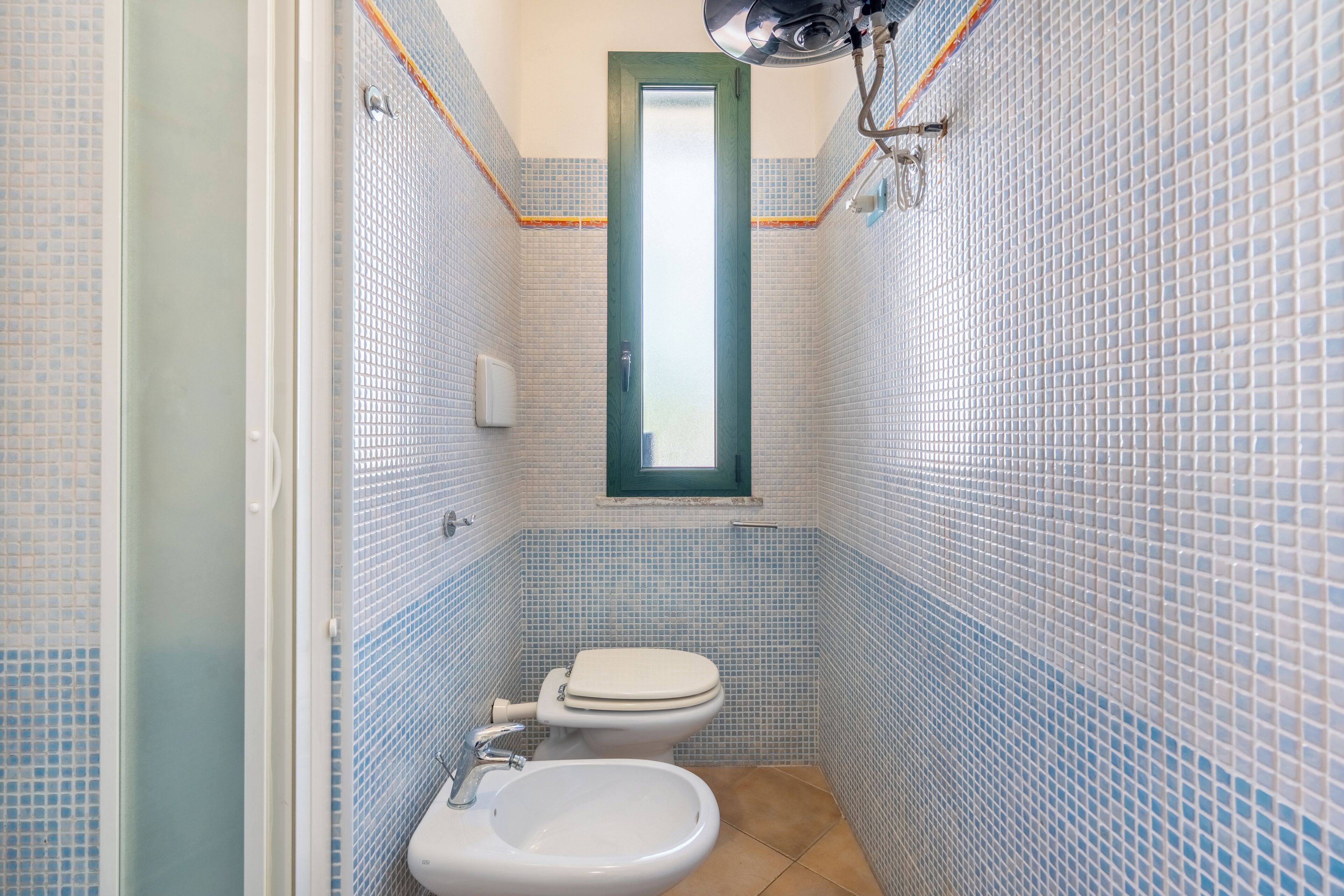 Un baño con inodoro, bidé y lavabo, con azulejos azules y blancos.