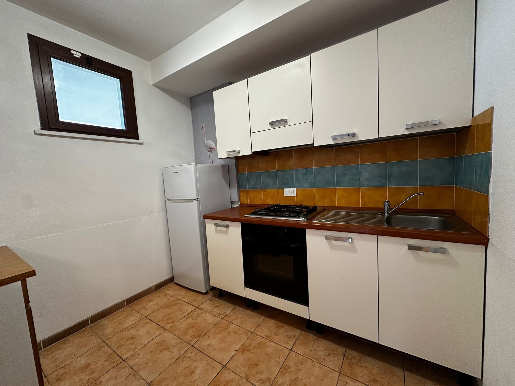 Una cucina compatta con mobili bianchi, piano cottura a gas integrato, lavello e frigorifero.