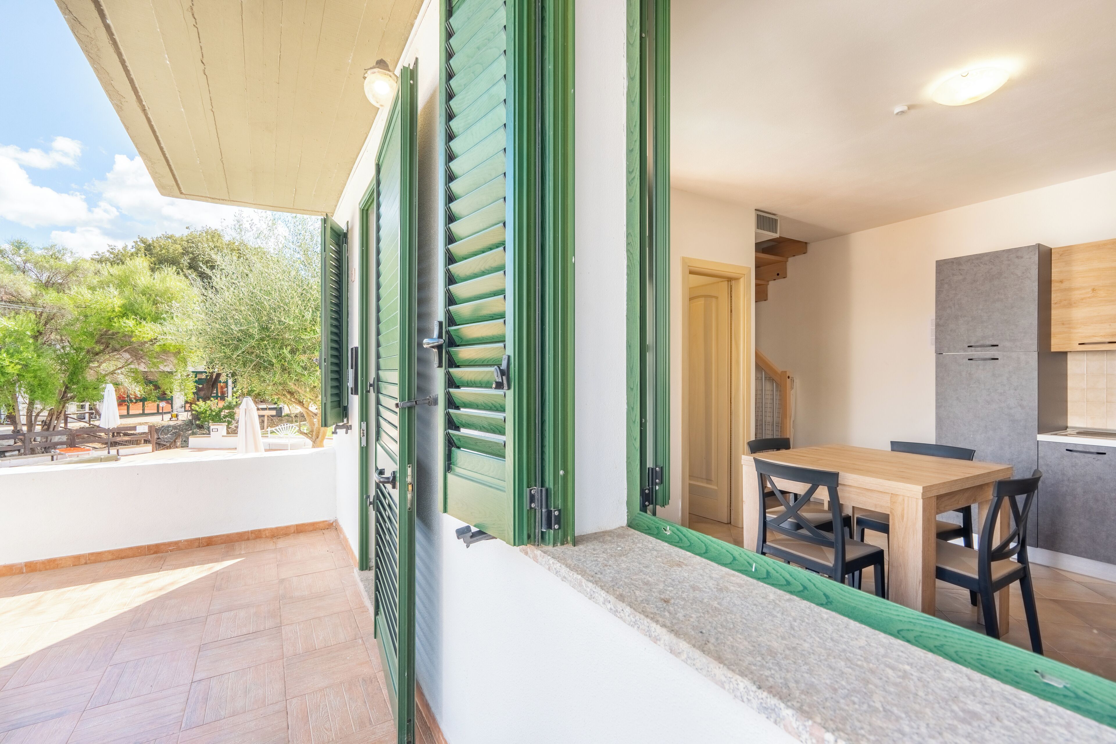 Un balcón con contraventanas verdes, una mesa de madera y sillas.
