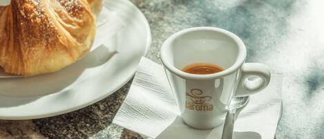 A croissant and a cup of coffee on a plate with a napkin, placed on a marble table.