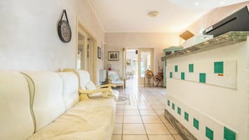 A hallway with a sofa, a wall clock, and a kitchen area with green and white tiles.