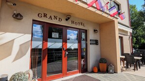 The exterior of the Grand Hotel with a red entrance door, a balcony with flags, and outdoor seating. - Grand Hotel Senica (Senica)