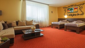 A hotel room with a sofa, two single beds, a coffee table, and a red carpeted floor. - Grand Hotel Senica (Senica)