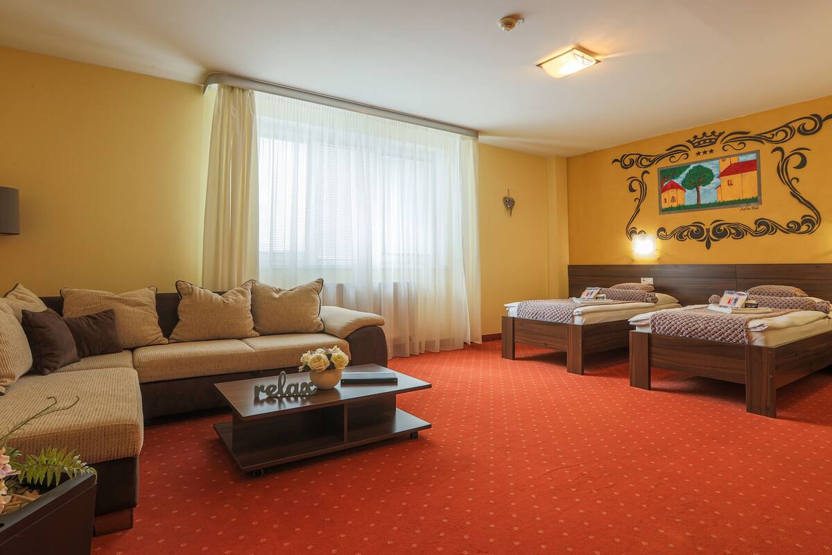 Una habitación de hotel con sofá, dos camas individuales, una mesita de centro y piso cubierto de alfombra roja.