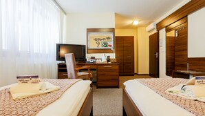 A hotel room with two beds, a desk, a chair, a television, and a wardrobe. - Grand Hotel Senica (Senica)