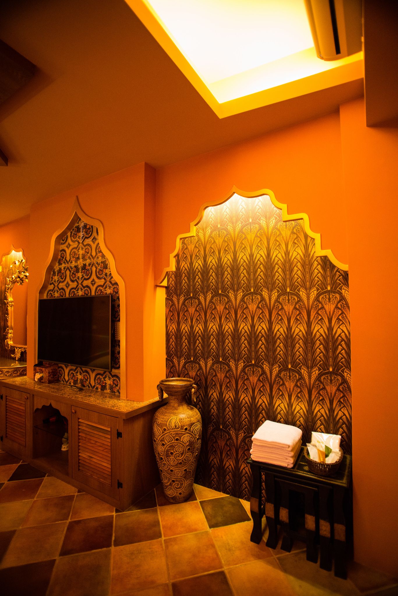 A room with a tiled floor, a wooden cabinet, a large vase, and a wall with intricate patterns.