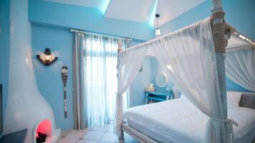 A bedroom with a canopy bed, a fireplace, a vanity with a mirror, and a wall-mounted light fixture.