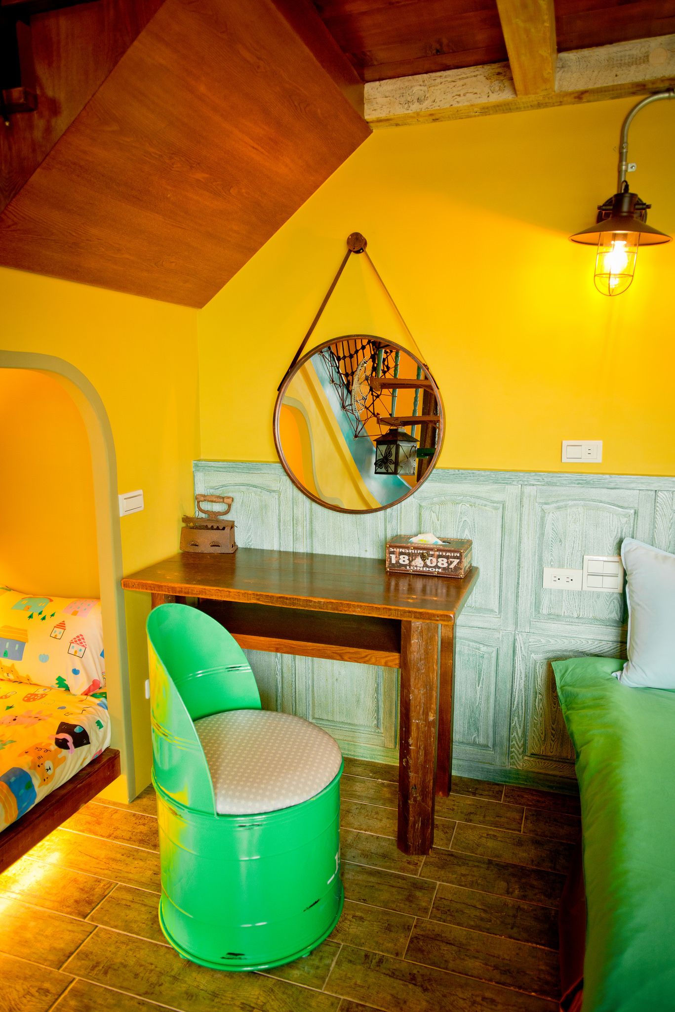 A cozy room with a wooden ceiling, a green chair, a wooden table, a hanging mirror, and a yellow wall.