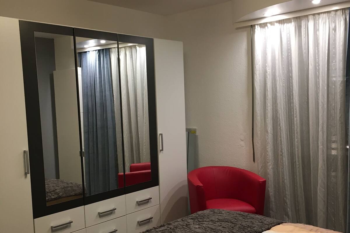Une chambre à coucher avec un lit, une chaise rouge, une armoire et un miroir.