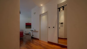 Un couloir doté d’un plancher en bois, d’une porte blanche et d’un miroir qui reflète une partie de la pièce.
