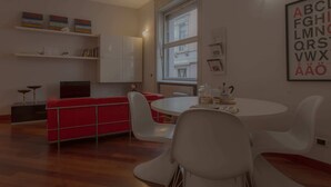 Un salon moderne avec un canapé rouge, des fauteuils blancs, une table ronde et une grande fenêtre.
