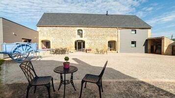 Un bâtiment en pierre avec un toit gris, une cour intérieure avec une table et des chaises, et une roue de voiture bleue.
