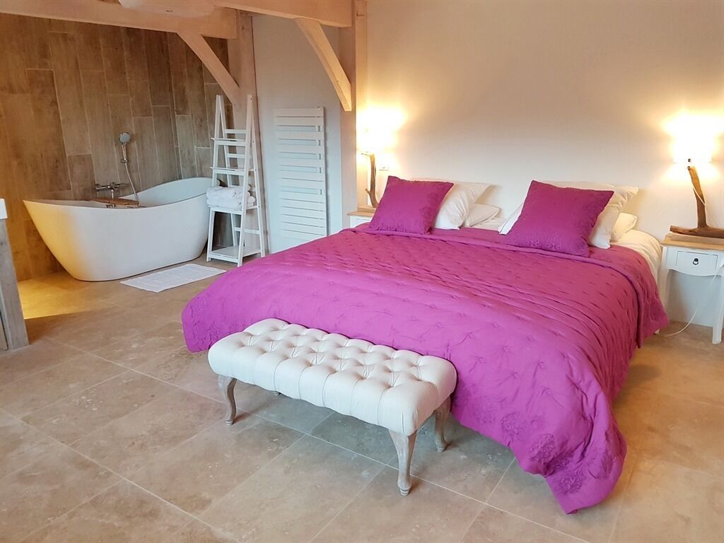 Un dormitorio con una cama grande, un banco, una bañera y una escalera.