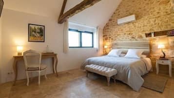 A bedroom with a stone wall, a bed with a headboard, a chair, a desk, and a window.