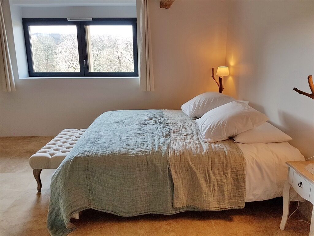 A bedroom with a bed, a nightstand, a lamp, and a window.