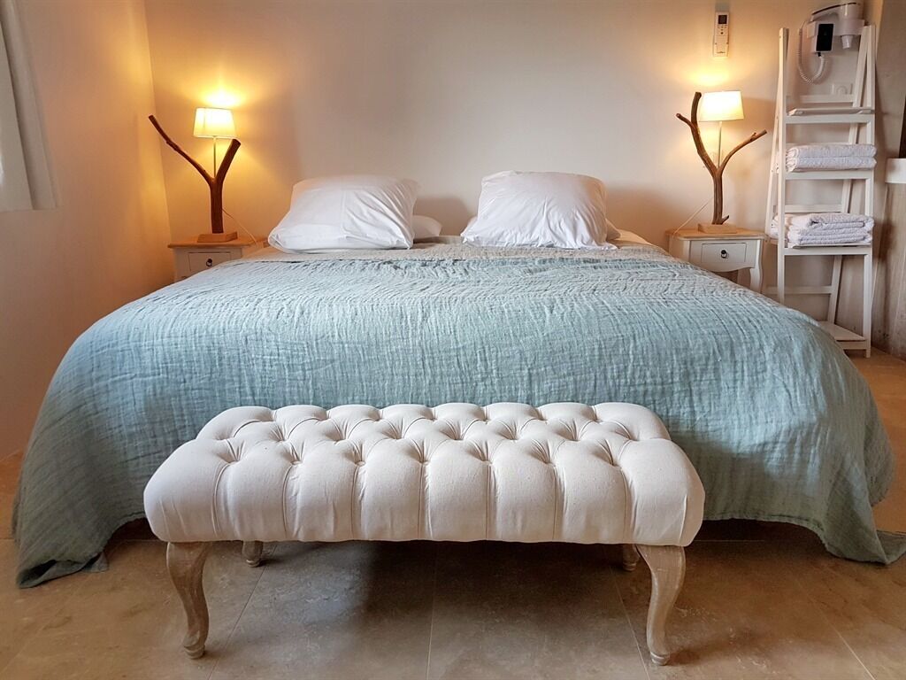 Une chambre bien rangée, avec un lit, deux tables de chevet, un banc et une échelle sur laquelle sont posées des serviettes.