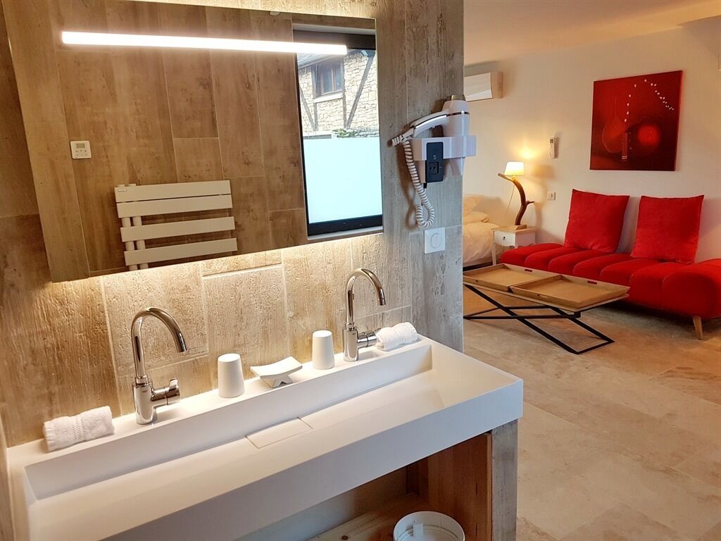 Un baño moderno con un lavamanos grande, un secador de pelo y un espejo. En la sala de estar, hay un sofá rojo y una mesa de madera.