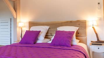 A bed with a wooden headboard, two white pillows, and two purple pillows. There are two bedside lamps on either side of the bed.