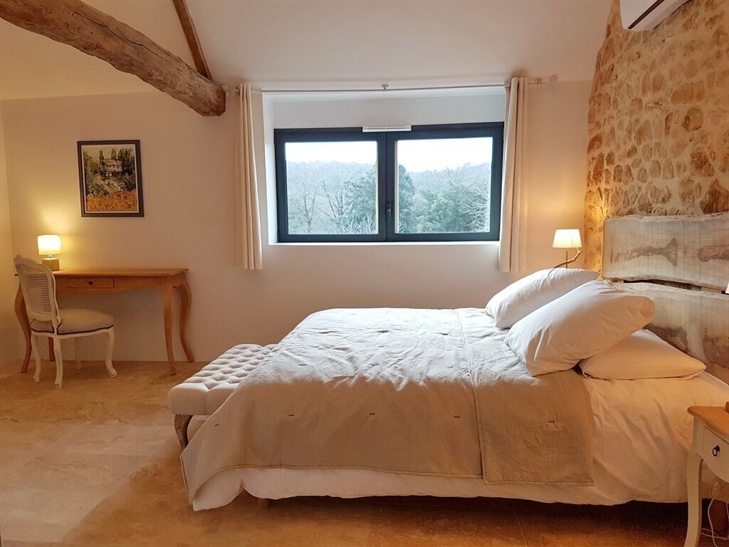 A bedroom with a bed, a desk, a chair, and a window with a view of trees.