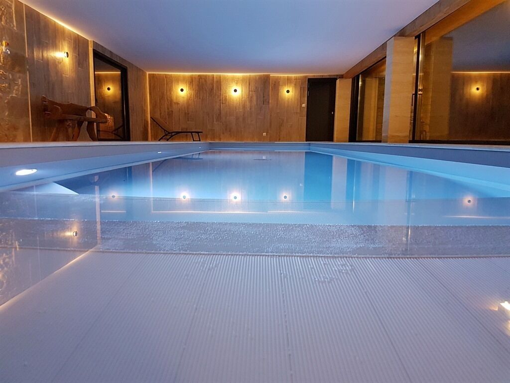 A modern indoor swimming pool with a wooden wall and recessed lighting.