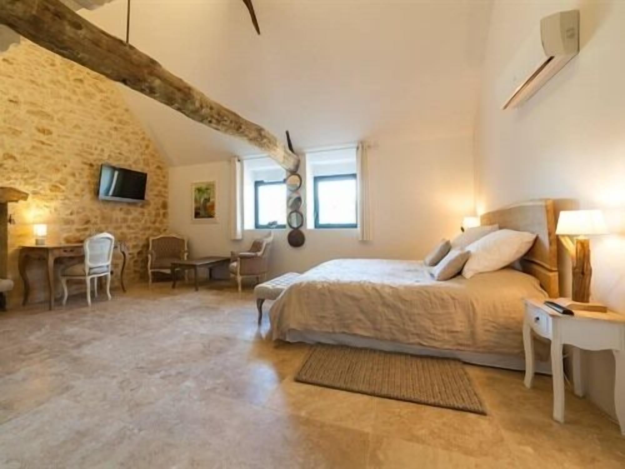 A cozy bedroom with a sloped ceiling, a bed with a headboard, a desk with a chair, and a television mounted on the wall.