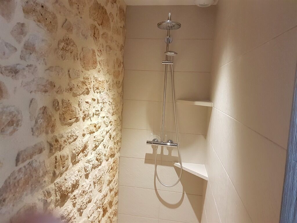Ducha con cabezal de ducha de mano y grifo empotrado en una habitación con paredes de piedra y suelo de baldosas.