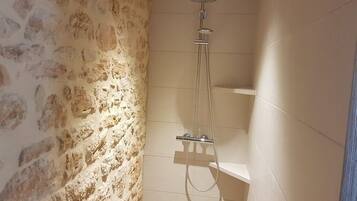 Ducha con cabezal de ducha de mano y grifo empotrado en una habitación con paredes de piedra y suelo de baldosas.