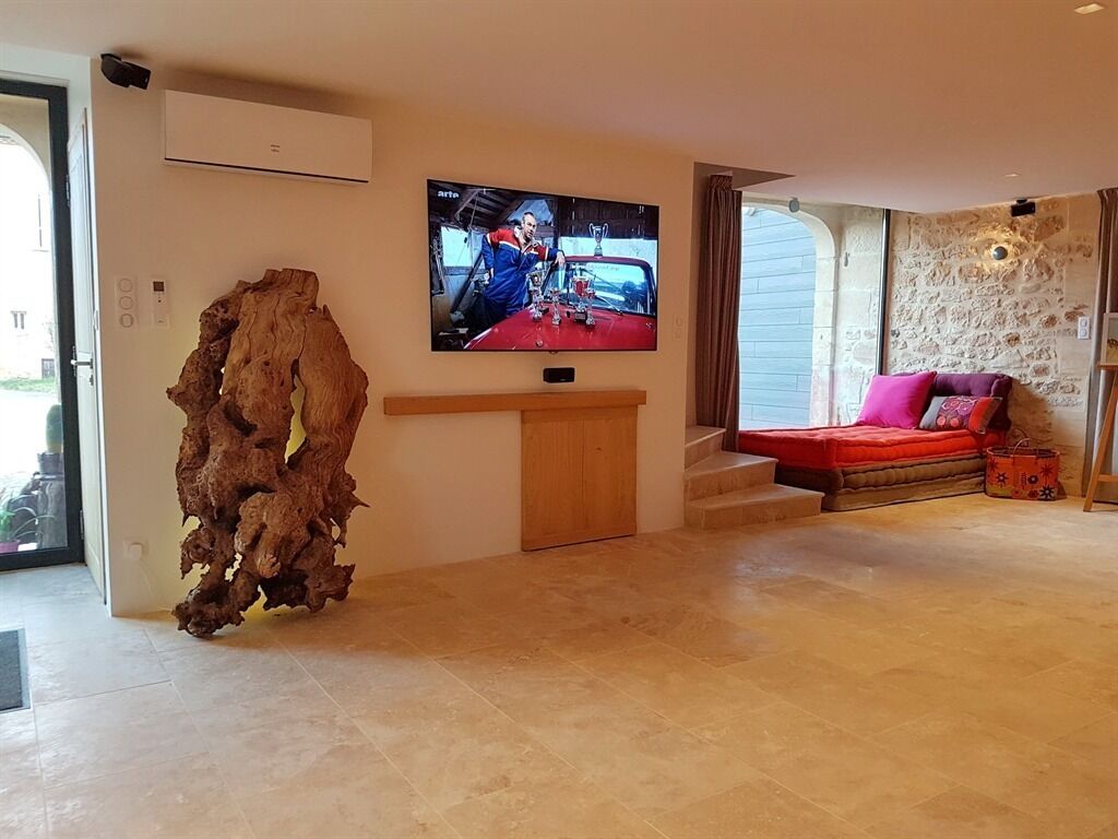 A living room with a television mounted on the wall, a wooden cabinet, a red sofa, and a stone wall.