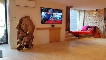 A living room with a television mounted on the wall, a wooden cabinet, a red sofa, and a stone wall.