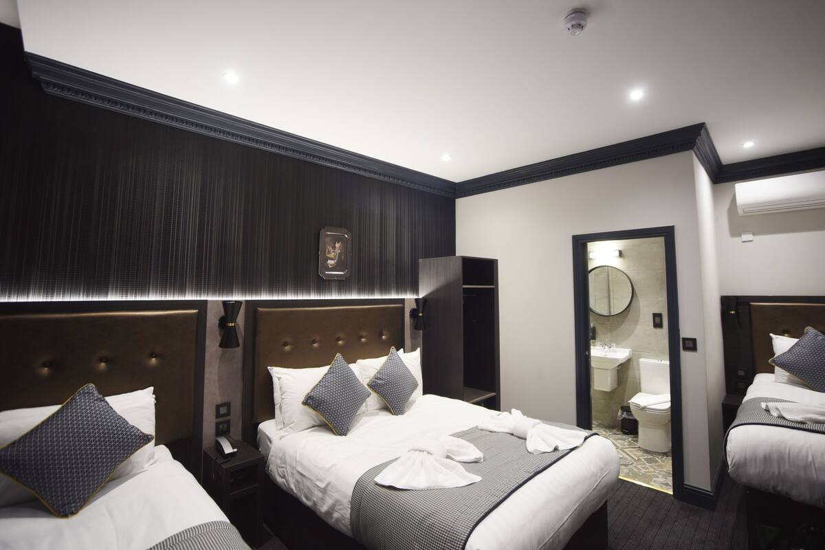 A hotel room with two beds, a large mirror, a bedside table with a phone, and a bathroom visible through an open door.