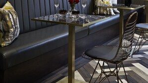 A modern dining area with a dark blue wall, a large framed painting, a glass table, and a leather booth. - House of Toby (London)