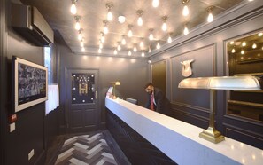 Zona de recepción de hotel con diseño moderno, que incluye un mostrador de recepción, un espejo grande y una pared decorativa con una cabeza de animal montada.
