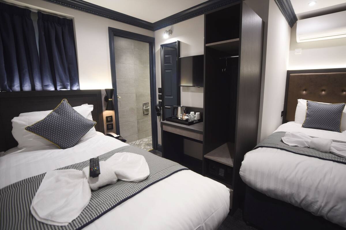 A hotel room with two beds, a minibar, a mirror, and a door leading to a bathroom.