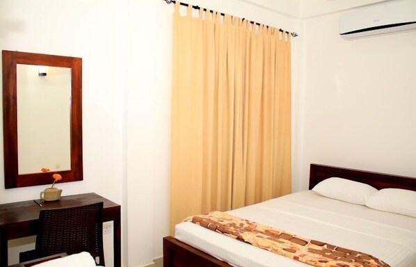 A hotel room with a bed, a wooden headboard, a bedside table with a lamp, and a large window with curtains. - Seasons Villa (Inamaluwa)