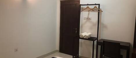 A hotel room with a bed, a desk, a chair, a wardrobe, and a towel rack.