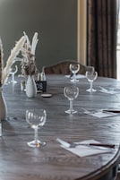 A wooden dining table with several wine glasses and a vase with dried plants.